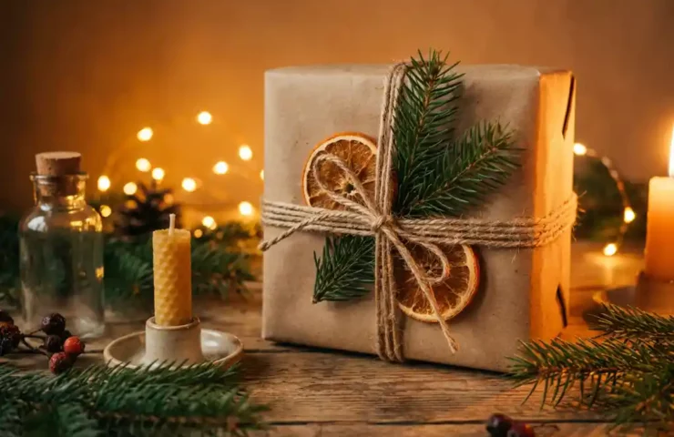 Duurzaam ingepakt cadeau met natuurlijk touw, omringd door dennentakjes, een handgemaakte kaars en glazen fles op rustiek houten tafel.